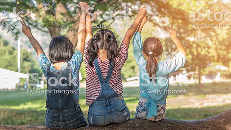 three kids sitting on a log holding hands up into the air