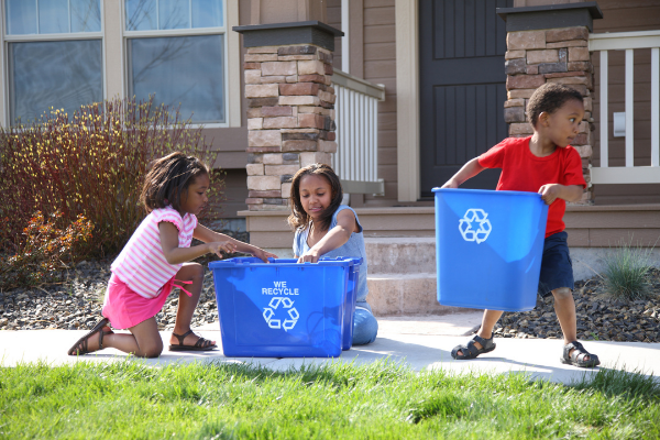 kids putting items in recycling bin outside a house
